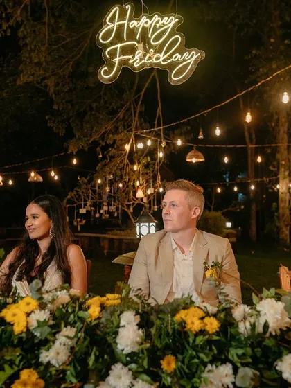 A fun "Happy Friday" neon sign adds a personal and playful touch to this floral-adorned head table at a wedding reception.