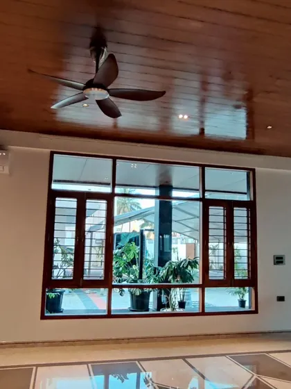 This room features a polished wood ceiling that adds warmth and reflects light. The large wooden window frame connects the interior with the green space outside.
