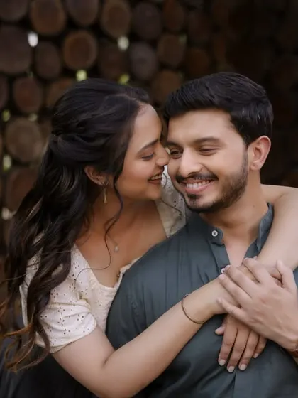 An intimate embrace against a rustic, wooden background. This shot captures the couple's easy chemistry, with their coordinated casual wear reflecting a comfortable and authentic style.