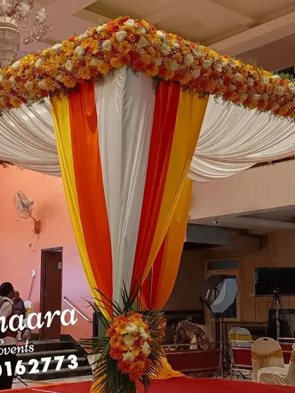 A classic wedding entrance with draped fabric in festive orange and yellow. The canopy is topped with marigolds, setting a traditional and welcoming tone for the celebration.