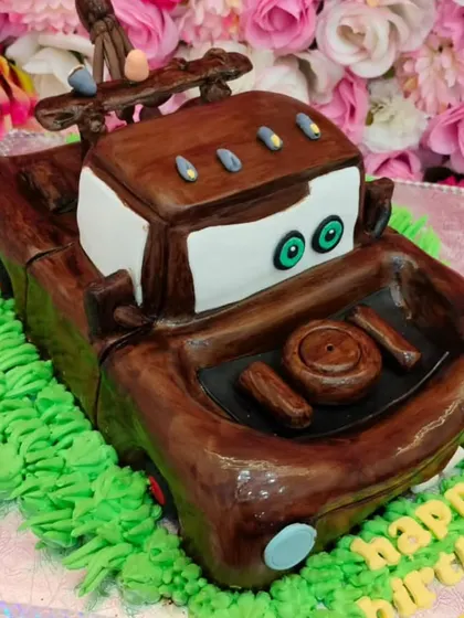 A fully sculpted 3D cake of Mater from the movie 'Cars'. This cake is made with rich chocolate ganache and filled with strawberry compote, showing that complex designs can also be delicious.