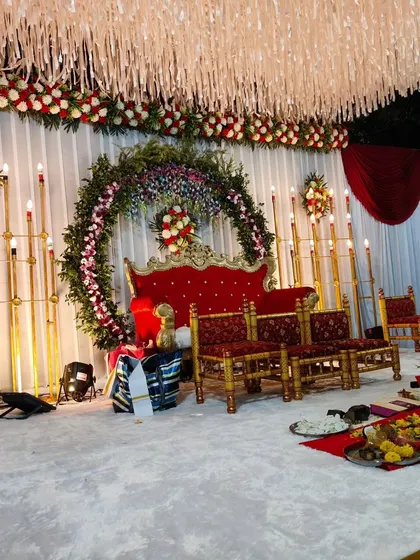 This is a setup for a wedding ceremony (vivah) with seating for the rituals. The stage features a large floral ring backdrop, traditional seating for the bride and groom, and all the necessary items for the puja.