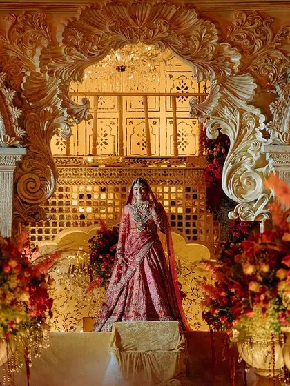 The bride, poised and regal, framed by the ornate arches of the stage. The design creates a perfect portrait moment, blending her beauty with the architectural splendor.