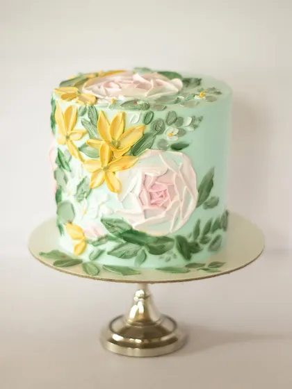 A floral painted cake in a lovely shade of teal. The soft green-blue background makes the pale pink and yellow flowers pop. This design is perfect for someone looking for something a little different from the usual pinks and whites.