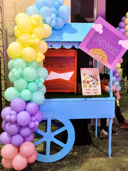 A close-up of the blue popcorn cart at the Candyland party, decorated with a rainbow of pastel balloons.