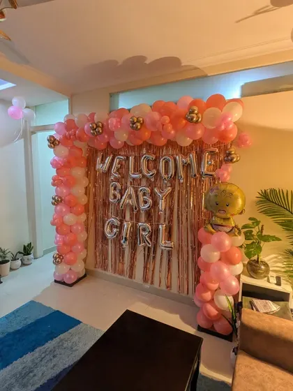 A full view of the living room space transformed for a baby girl's arrival, showing the main backdrop and coordinated balloons throughout the room.