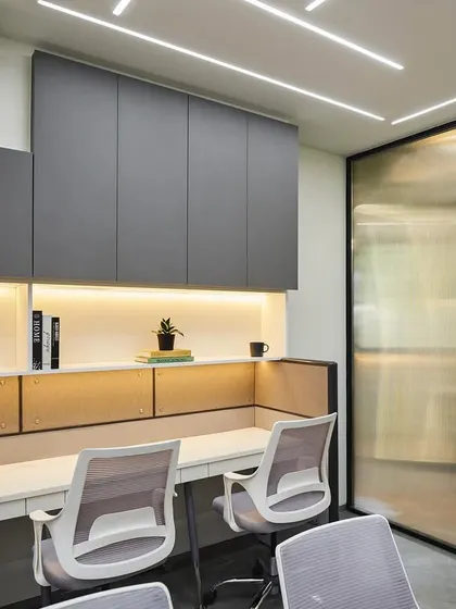 A closer look at the workstation design. Fluted glass partitions offer a sense of personal space without closing off the area, complemented by ample overhead storage in a sleek grey finish to maintain a clutter-free environment.