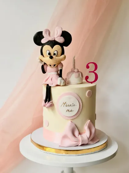 An elegant Minnie Mouse cake for a third birthday. The hand-sculpted, full-figure Minnie sits atop a classic buttercream cake, accented with a simple pink bow and polka dots.