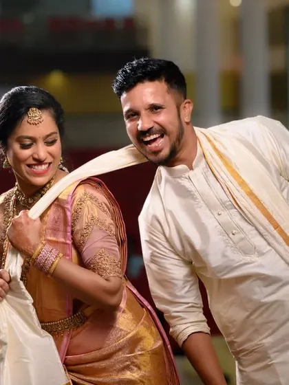 A fun, candid moment from a wedding event. The groom playfully pulling on the bride's saree captures their personalities and the joy of the day.