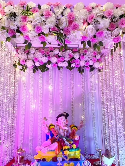 This setup features a canopy of pink and white flowers with curtains of hanging floral strings and fairy lights. The purple lighting gives the entire mandap a magical glow.