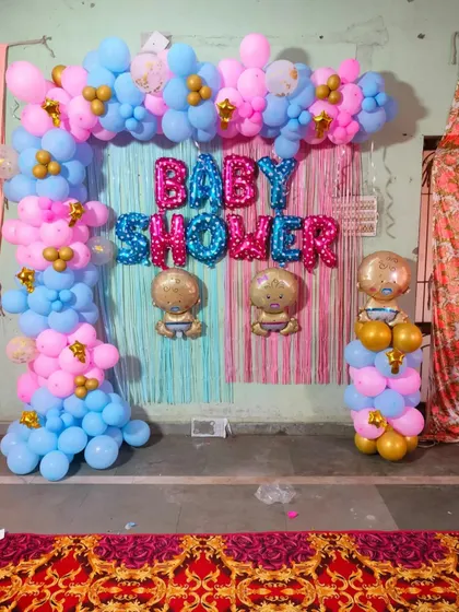 A classic 'Baby Shower' backdrop for a home celebration. This setup uses a pink and blue theme with a tinsel curtain, foil letter balloons, and baby-shaped character balloons.
