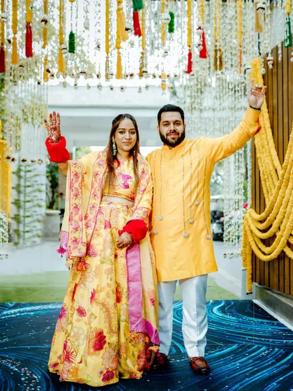 The couple makes a grand entrance at their Haldi ceremony, waving to guests under a beautiful floral decor.
