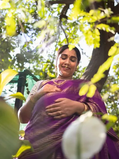 A creative shot looking up at the mother-to-be through lush green leaves, with sunlight filtering through, creating a natural and organic feel.