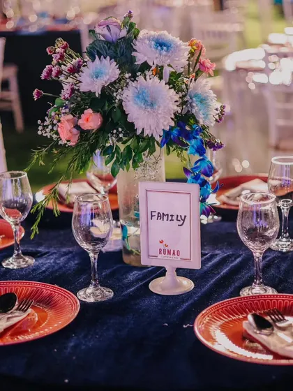 A vibrant table setting with a rich blue velvet tablecloth and contrasting red plates. The colorful floral centerpiece and custom "Family" table sign add a personal and lively touch.