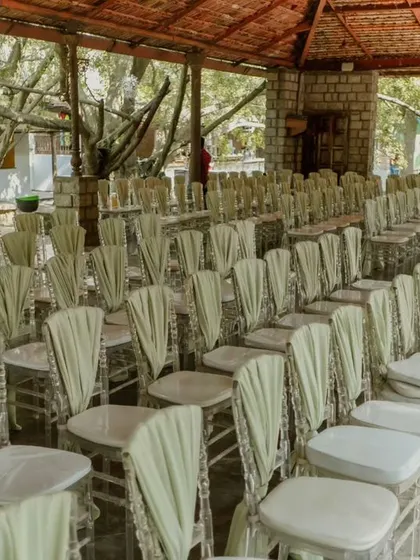 Guest seating for a wedding ceremony, with elegant clear chairs adorned with flowing sage green sashes.