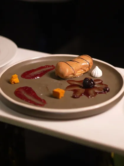 An artfully deconstructed eclair. The choux pastry is presented alongside smears of jam, cubes of fruit, and a single meringue, inviting the guest to experience the classic dessert in a new way.