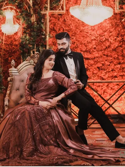 A royal and romantic portrait of the couple seated against a lavish red floral wall. The opulent setting and their elegant pose create a truly luxurious feel.