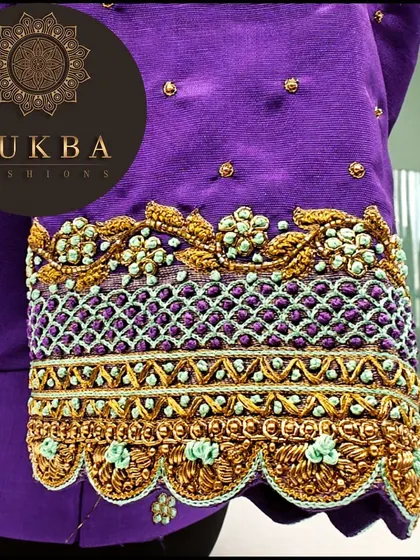 A close-up shot of the embroidery on a purple sleeve. You can see the detailed lattice work created with gold thread and the delicate floral motifs in a contrasting mint green.