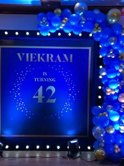 An elegant and modern setup for a 42nd birthday party. The deep blue and gold theme, complete with a custom digital backdrop and a stylish balloon arch, is perfect for a sophisticated celebration.