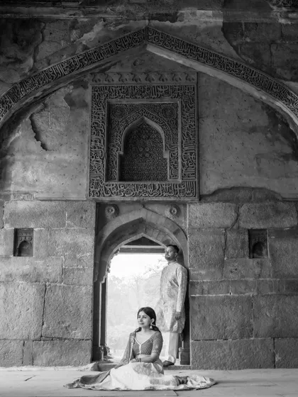 A classic black and white portrait of a couple at a heritage site. The composition highlights the intricate details of the architecture while keeping the focus on their elegant pose.