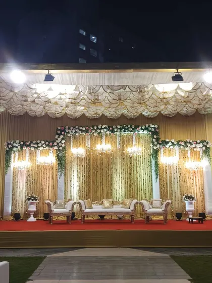 A grand, traditional reception stage with gold and white decor, featuring elegant sofas and chandeliers.