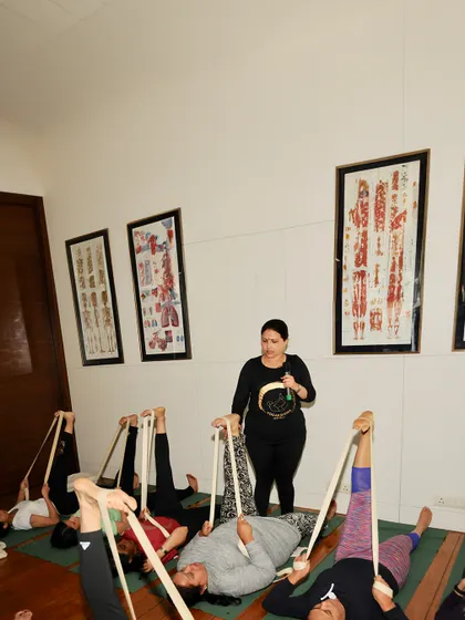 A class of students practicing supine leg stretches, with me providing guidance. The use of props ensures that everyone can work at their own level.
