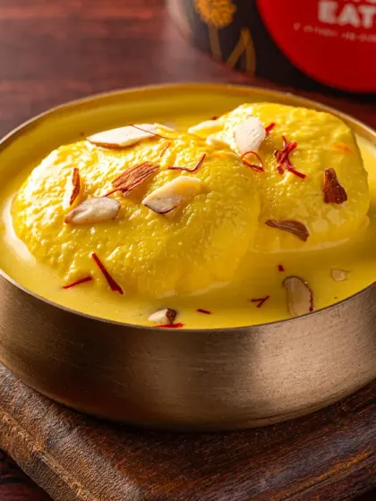 A close-up of Rasmalai for Charcoal Eats, garnished with saffron and almonds. This dessert photography focuses on the rich, creamy texture, making it an irresistible add-on for online orders.