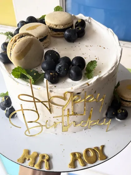 An elegant and minimal cake topped with fresh blueberries and macarons. The clean white design is perfect for a sophisticated celebration.