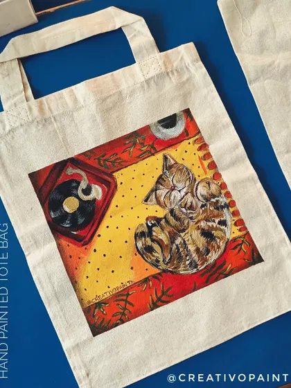 Here's a custom hand-painted tote bag for a fellow cat lover. I painted this cozy scene of a cat napping next to a record player, creating a unique, wearable piece of art that's both stylish and personal.