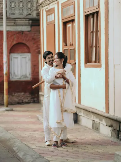 A warm embrace from behind in a quiet city lane. The traditional white outfits and old buildings give this a classic, romantic vibe.