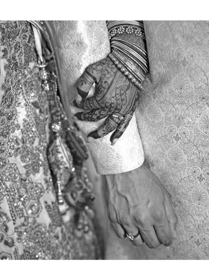 Another artistic black and white photo, focusing on the bride's mehendi-adorned hand resting on her partner's arm. The detailed henna work stands out, even without color.