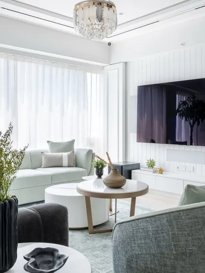 A wide view of the luxury living room, showcasing the calming blue and pastel palette. The design integrates a plush tufted sofa, accent chairs, and a statement chandelier with crystal and feather detailing.