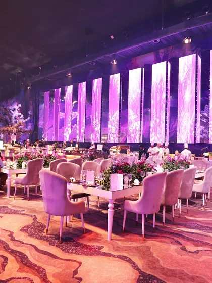 A wide view of a lavish event space, showcasing multiple seating arrangements and our strategically placed food stations. We are equipped to handle large crowds while maintaining an atmosphere of exclusivity and comfort.