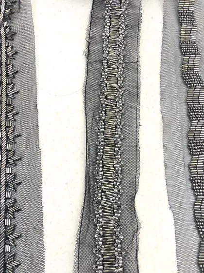 A trio of hand-beaded trims on a net base. Each lace features a unique pattern using metallic bugle beads, showcasing the variety of modern, linear designs available for couture embellishment.