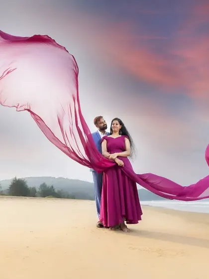 The full expanse of a dramatic beach scene. This wide shot captures the couple against a stunning sky, with the flowing fabric adding a sense of grandeur to their pre-wedding portrait.
