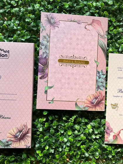 A modern wedding invitation set with a vibrant floral print on a soft pink background. The design includes a matching envelope and a separate insert for the ceremony details, all tied together with a custom monogram.