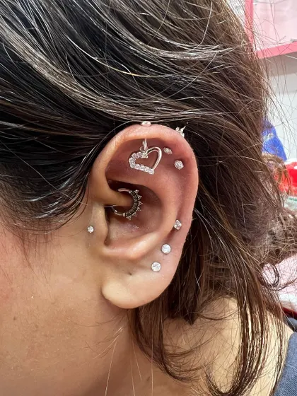 A fully loaded ear stack featuring a heart-shaped hanging, a daith hoop, and a constellation of solitaire studs running up the ear.