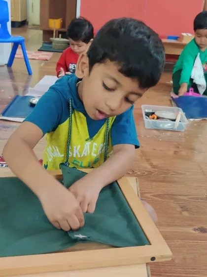 The button frame requires immense concentration and dexterity. Here, a child is working diligently to master the skill of buttoning, a practical life exercise that prepares them for dressing themselves and develops pincer grasp.