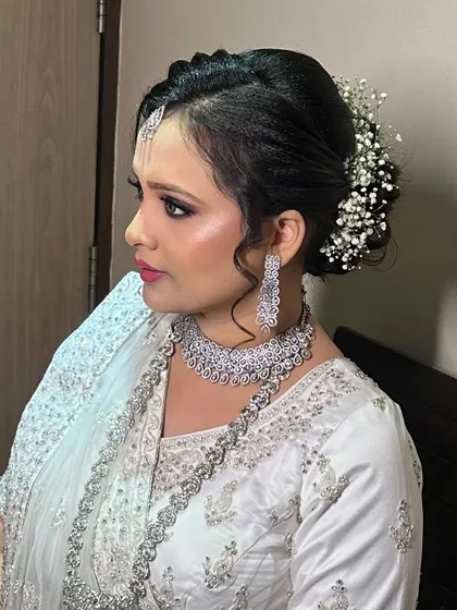 A side profile of my client for her reception. The elegant braided bun is adorned with baby's breath, and her makeup is a sophisticated look with smoky eyes, paired with a stunning diamond necklace.