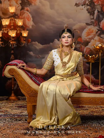 A model seated on a divan, looking like a queen in a golden Kanjeevaram saree and a contrasting white blouse with heavy gold embroidery.
