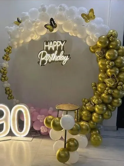 An elegant 90th birthday setup with a white and gold balloon ring, butterfly accents, and a large '90' marquee number.