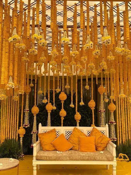 A classic Haldi ceremony backdrop, featuring dense strings of vibrant yellow marigolds. This traditional floral decoration creates a beautiful and auspicious setting for the event.