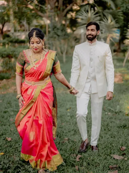 A more formal walking pose, perfect for showcasing the full wedding outfits. The bride's elegant Kanjeevaram saree and the groom's classic white suit create a stunning visual.