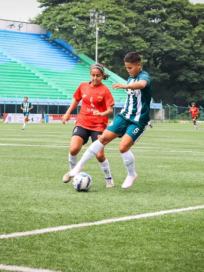 A player shields the ball effectively, using her strength to hold off a challenge from an opponent in a red jersey.