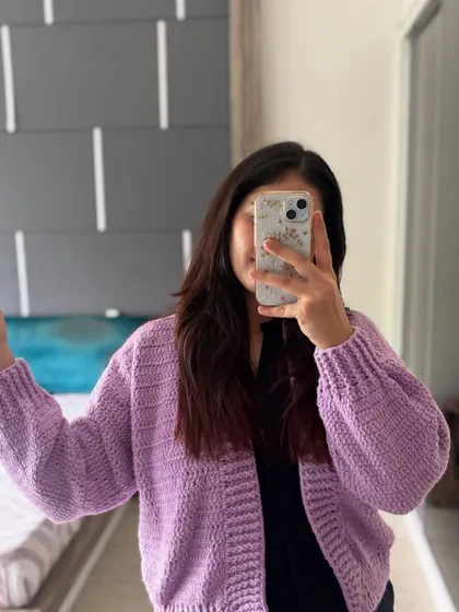 This is a mirror selfie showing the fit of our Plum Puff Cardigan in lavender. It has a comfortable, slightly oversized feel that fits a range of sizes from S to XL.
