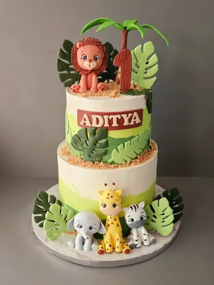 A two-tier jungle cake for Aditya's first birthday. This blueberry cake features a variety of hand-sculpted fondant animals, including a lion, elephant, giraffe, and zebra.