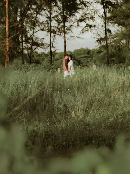 A couple stands together in a field of tall grass, sharing a quiet, intimate moment. This photo captures the feeling of finding your own world together, surrounded by nature.