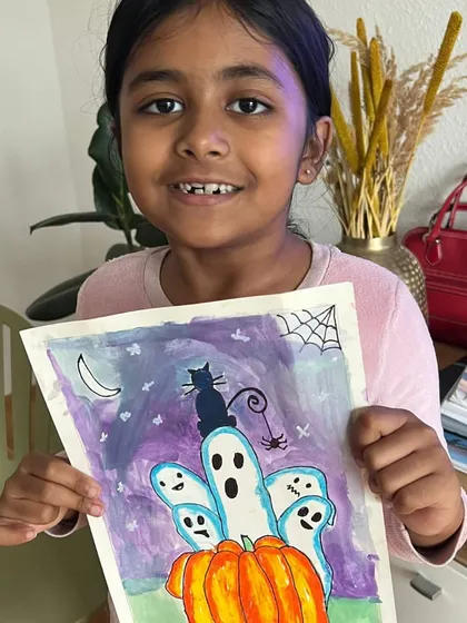A proud online student holding up her Halloween painting of friendly ghosts and a black cat sitting on a pumpkin. So creative and cute.