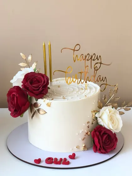 An elegant birthday cake with red and white roses, gold leaves, and a beautiful script topper.