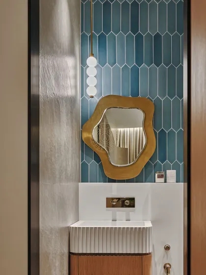 We brought the brand's signature blue into the bathroom with these playful, vertically stacked subway tiles. An asymmetrical, brass-framed mirror adds a fun and fresh element to the space.